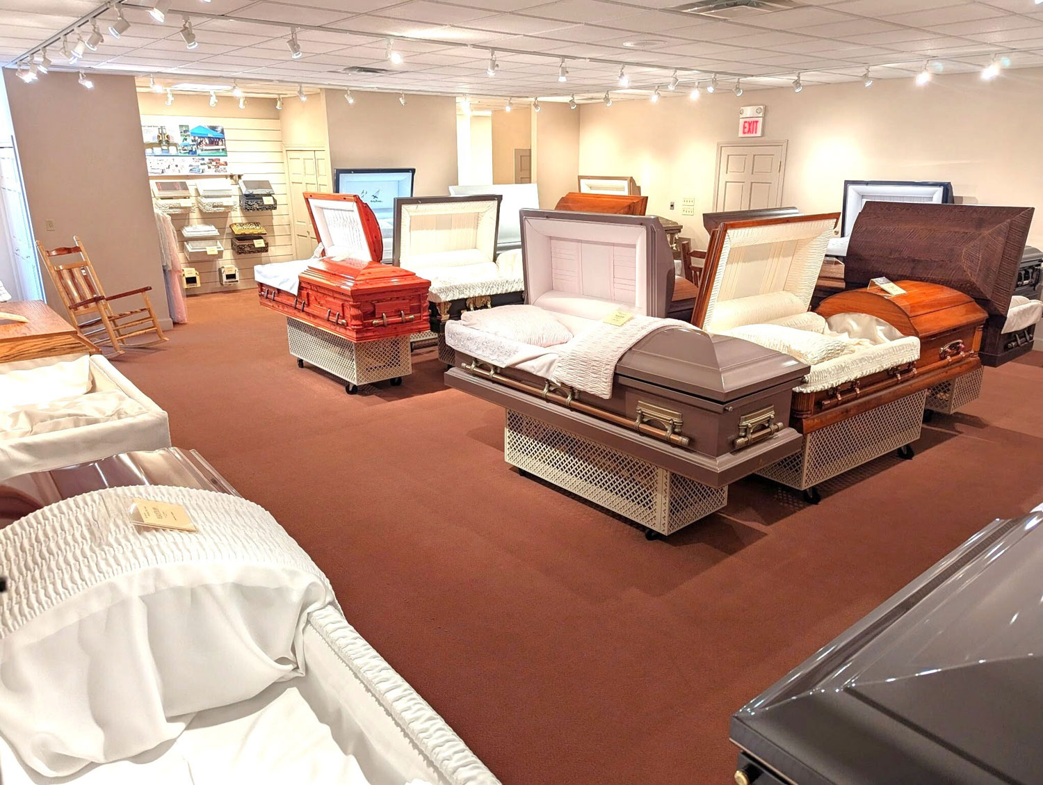 Various selections of caskets in the room with the other funeral merchandise displayed on the wall.